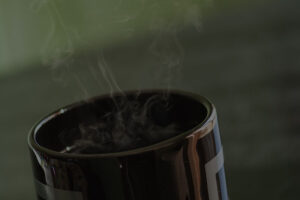 Black cup of coffee with steam rising from within it.